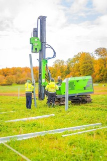 Two workers set up posts in a meadow with a drilling rig, Energiewende, construction of PV open