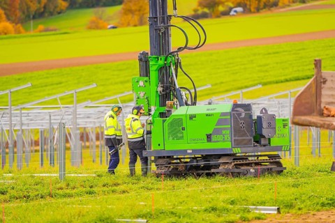 Workers in safety vests monitor the installation of metal structures in an open field,