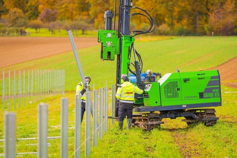 Green machine and worker installing metal poles in the field on a sunny autumn day, Energiewende,