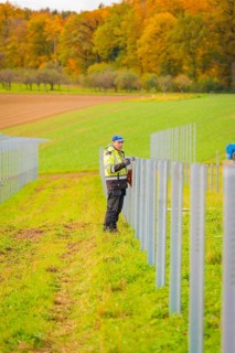 Worker attaches a pole in a row of fields surrounded by colorful autumn leaves, energy revolution,