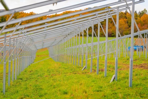 A long metal framework runs on a green field in autumn, surrounded by trees, energy transition,