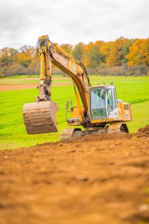 Excavator lifts soil in a green landscape with autumn trees, energy revolution, construction of PV