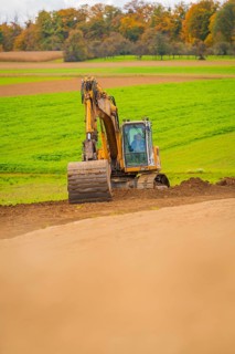 Excavator works on a hill in a green field in autumn, energy revolution, construction of PV open