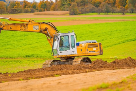 Large yellow excavator operating on an open, green area, energy revolution, construction of PV open