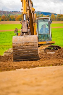 An excavator lifts soil on a field with a green landscape and a hilly background, Energiewende,