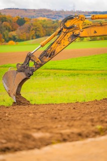 Close-up of an excavator bucket moving earth surrounded by green fields, energy transition,