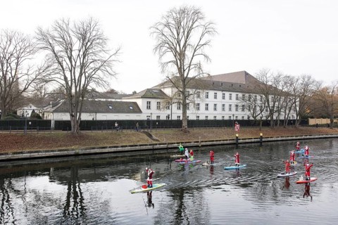 Water sports enthusiasts dressed up as Santa Claus ride SUPs on the Spree in front of Bellevue