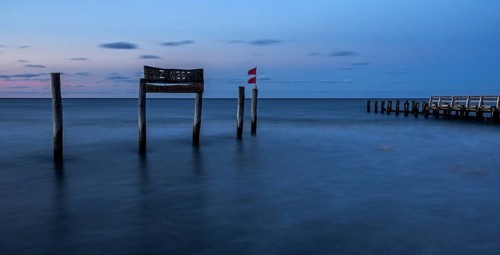 Wooden sign in the sea with inscription Zingst and wooden walkway, long exposure, evening light,