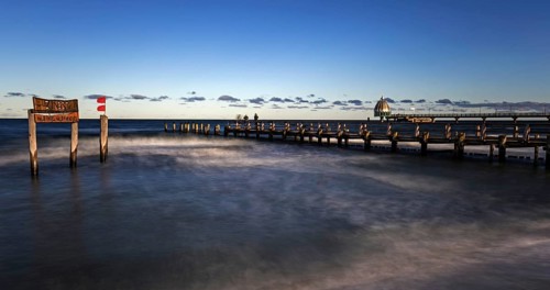 Wooden sign in the sea with inscription Zingst and wooden walkway, pier with diving gondola behind,