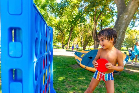 Young boy concentrating on playing a giant connect four game in a park on a summer day, holding a