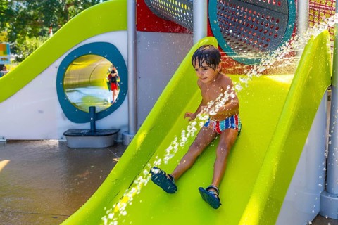 Happy child enjoying a sunny summer day, sliding down a bright green water slide at a splash park,