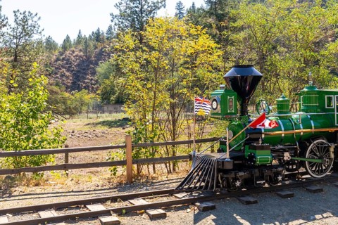 Green miniature train with canadian and british columbian flags stands on tracks in kamloops,