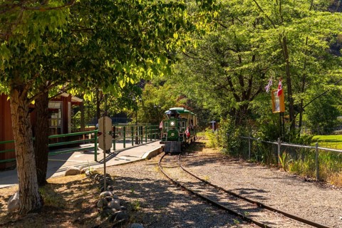 Green and yellow miniature train approaching the station in a sunny summer day in kamloops, british