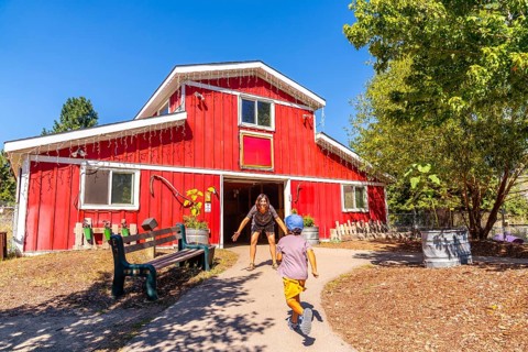 Child runs towards their mother who is waiting with open arms in front of a bright red barn at the