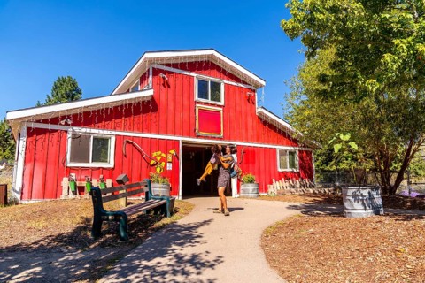 Mother carrying her young daughter as they are leaving a vibrant red barn at the british columbia