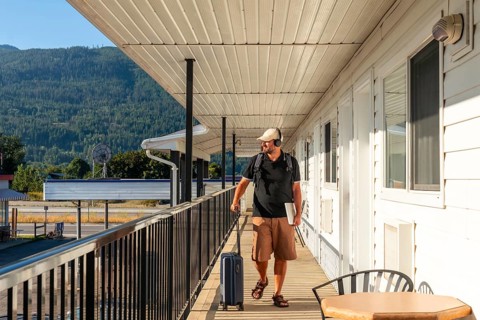 Digital nomad walking along a motel balcony, surrounded by luggage and a laptop, soaking in the