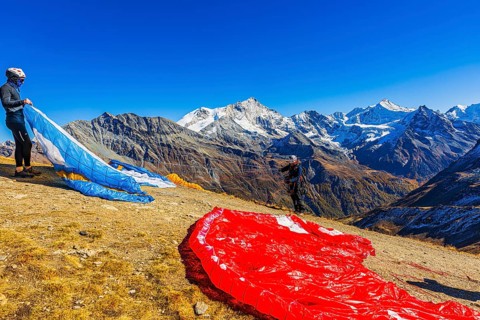 Paragliders are preparing for their start, with the snow-capped peaks of the Valais Alps, Val