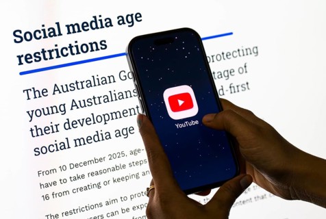 In this photo illustration, a person holds a phone displaying the YouTube app in front of a screen