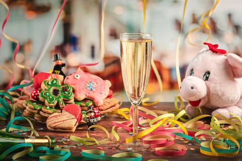 Filled champagne glass surrounded by New Year cookies, streamers and plush pig