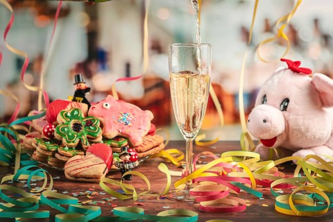 Pour sparkling wine into glass surrounded by New Year cookies, streamers and a plush pig