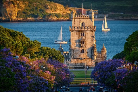 Scenic view of Belem Tower in Lisbon, Portugal, seen over a street with blooming purple jacaranda