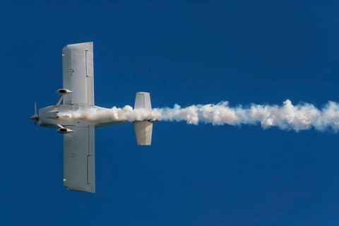 Stunt aerobatic plane performing stunts in blue sky with smoke trail. Concept of speed, difficulty,