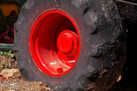Close-up and rear side view of large heavy duty black rubber tire mounted on red rim on monster
