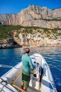 Young man rides a motorboat along the picturesque rocky coast, cliffs and blue sea, Golfo di