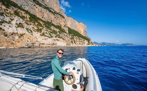 Young man rides a motorboat along the picturesque rocky coast, cliffs and blue sea, Golfo di