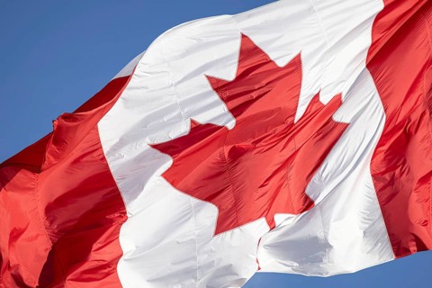 Red and white Canadian flag with a maple leaf waving in the air in downtown Toronto near Ontario