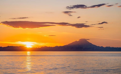View of Cook Inlet on white mountain peaks of Mount Redoubt at sunset, picturesque golden light of