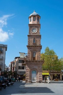A tall clock tower in an urban square with trees and shops, Çanakkale Clock Tower, Canakkale,