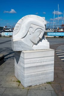 A marble sculpture with the inscription 'Troia' on the harbor, boats in the background, Çanakkale,