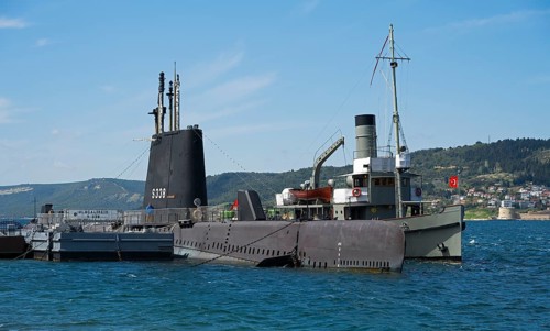 Submarine and ship in harbor overlooking a distant city and hills, TCG Uluçalireis S-338, War