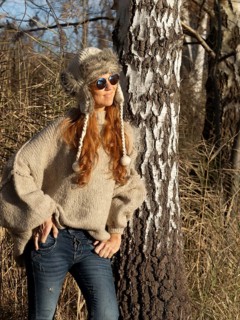 Slender pretty woman with fur hat and pompoms, red hair and warm winter colors between birch forest