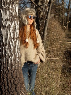 Slender pretty woman with fur hat and sweater, red hair and warm winter colors between birch forest