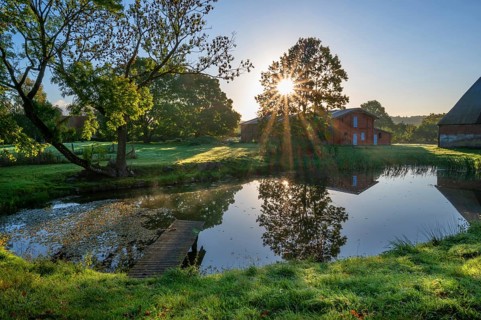 Manor with historic stables and pond, from 1923, in backlight with sun star, Gut Othenstorf,