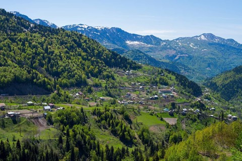 A small town is nestled in a green mountain landscape under clear skies, village in the Lesser