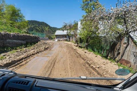 A rural road seen from a car surrounded by blooming trees and a country house, campers on a