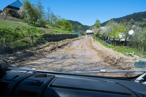 A muddy country road is viewed from a driving perspective through a car window, campers on a