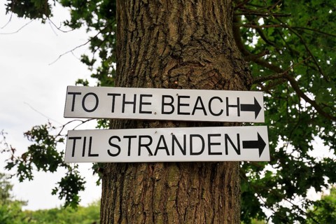 Bilingual signs with inscription, direction sign to the beach on a tree, Galløkken Strand, Rønne,