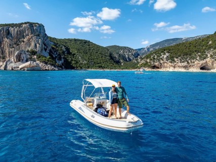 Couple, young woman and young man on motor boat off picturesque rocky coast, cliffs and Cala Luna