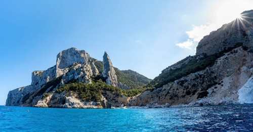 Picturesque rocky coast, cliffs with L'Aguglia pinnacle, blue sea and Cala Goloritzé beach, sun