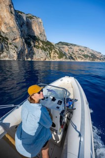 Young woman riding a motorboat along the picturesque rocky coast, cliffs and blue sea, Golfo di