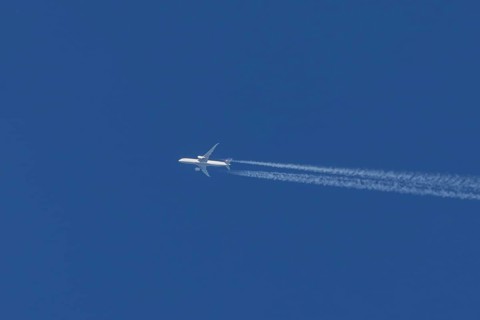 Jet passenger aircraft flying in a blue sky with contrails or vapour trails behind, England, United