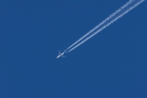 Jet passenger aircraft flying in a blue sky with contrails or vapour trails behind, England, United