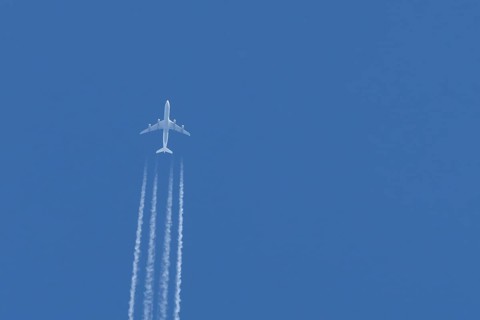 Jet passenger aircraft flying in a blue sky with contrails or vapour trails behind, England, United