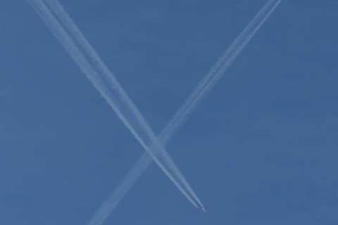 Aircraft contrails or vapour trails crossing in a blue sky, England, United Kingdom