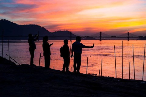 People enjoy the vibrant sunset by the Brahmaputra riverside, capturing photos and moments against