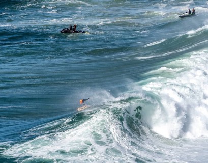 Surfers with their jet ski pilots in the Atlantic waves below Farol de Nazaré, Forte São Miguel,